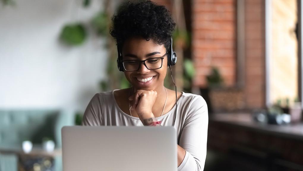 A woman wearing headphones and smiling while working on a laptop.
