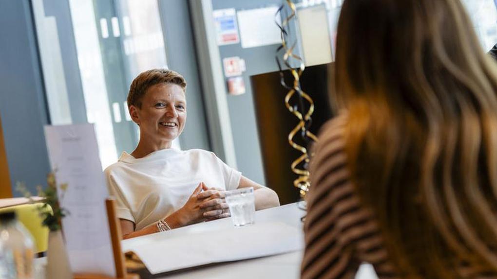 Mayor of Greater Manchester Bev Craig sits across the table, smiling at a student who has her back to the camera and is talking to the Mayor.