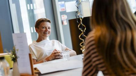 Mayor of Greater Manchester Bev Craig sits across the table, smiling at a student who has her back to the camera and is talking to the Mayor.