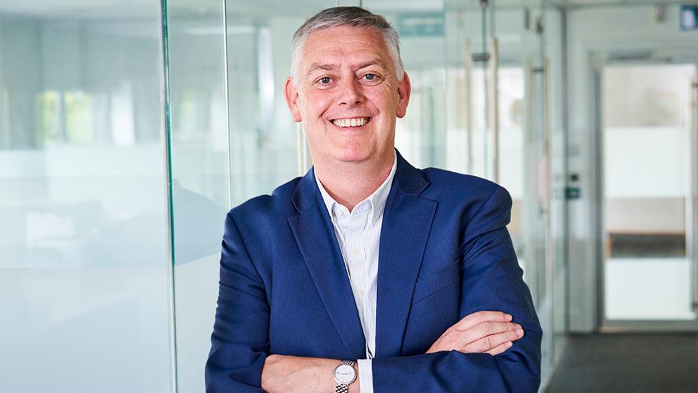 LTE Group CEO John Thornhill is leaning against a glass door with his arms folded and smiling into the camera.